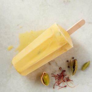 A creamy yellow popsicle with saffron threads and lime slices.