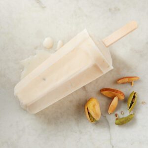 A wooden popsicle mold with frozen popsicle and spices around it.