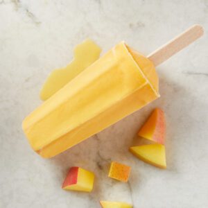 A yellow popsicle with melon pieces on a white background.