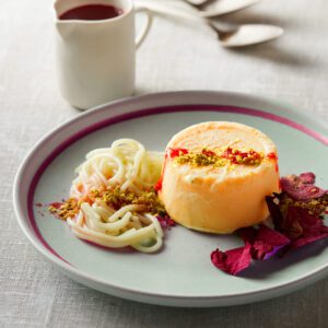 Elegant dessert plate with flan, cream, and fruit sauce.